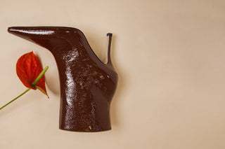 Brown patent leather boot with a red anthurium flower on a beige background