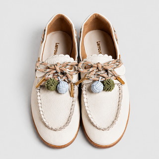 Pair of white moccasin-style shoes with decorative laces and colorful tassel details, photographed from above on a light gray background.
