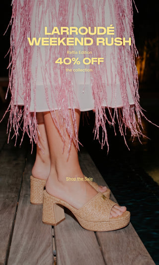 Model wearing woven raffia platform mule sandals with block heels, standing beside a pool. Promotional banner advertising a 40% discount on the raffia collection.