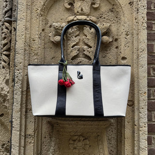 Larroudé women's canvas tote bag with black leather handles and trim, styled against a historic stone facade.
