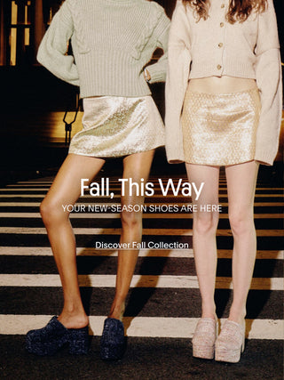 Two women wearing new-season Larroudé shoes and fall looks while standing on a city crosswalk at night.