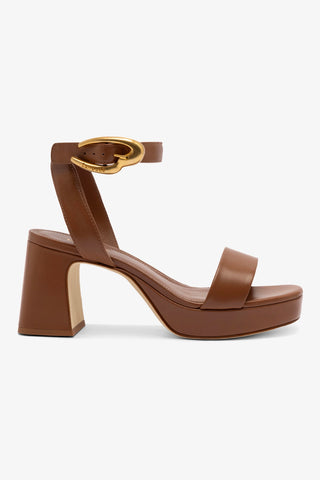 A caramel brown leather sandal with an ankle strap, golden hardware, and a block heel.