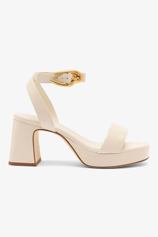 An ivory leather sandal with an ankle strap, gold hardware, and a low block heel.
