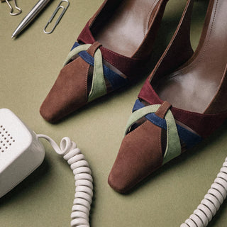 Larroudé suede pumps with a pointed toe and multicolor woven straps displayed on a desk beside office accessories.