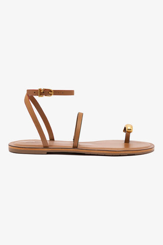 A light caramel colored flat sandal with gold hardware and an adjustable ankle strap.