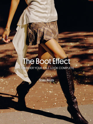 Woman wearing black croc-embossed Larroudé knee-high boots with a fall outfit on a sunlit city street.